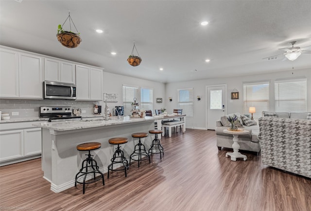 kitchen with backsplash, appliances with stainless steel finishes, open floor plan, light wood-type flooring, and a kitchen bar