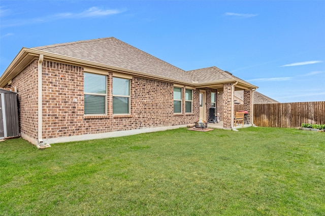 rear view of house featuring a yard, a shingled roof, fence, and brick siding