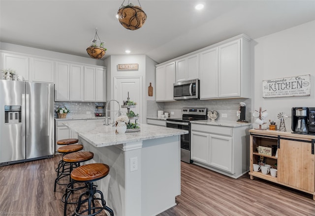 kitchen with a center island with sink, white cabinets, a breakfast bar area, wood finished floors, and stainless steel appliances