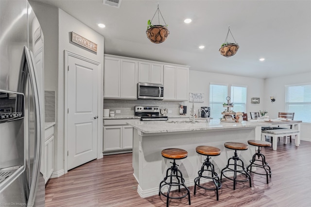 kitchen with light wood finished floors, stainless steel appliances, decorative backsplash, white cabinets, and a kitchen breakfast bar