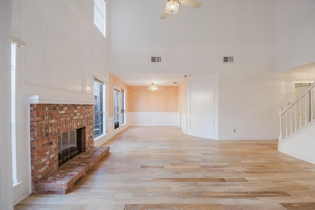 unfurnished living room featuring light wood-type flooring, a brick fireplace, stairs, and visible vents