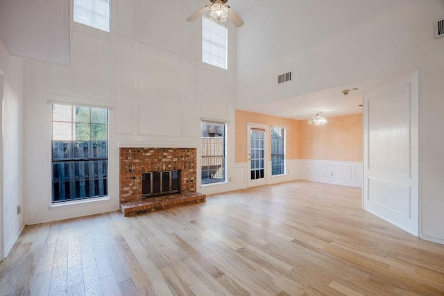 unfurnished living room with light wood finished floors, a brick fireplace, visible vents, and a decorative wall