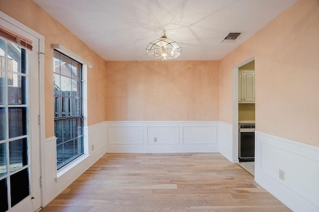 unfurnished room with light wood finished floors, visible vents, a chandelier, and a wainscoted wall