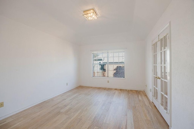 spare room with light wood-style flooring, baseboards, a raised ceiling, and french doors