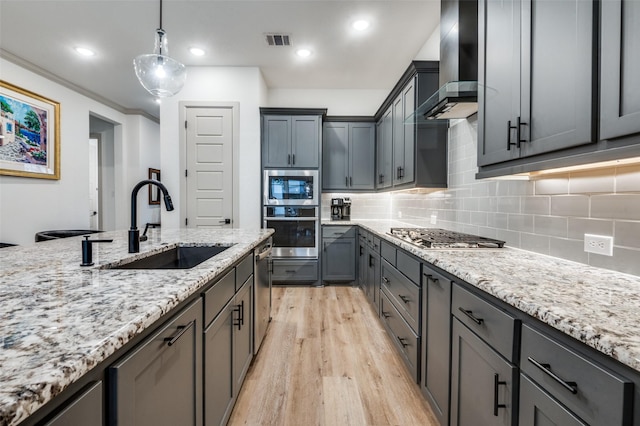 kitchen featuring visible vents, decorative light fixtures, stainless steel appliances, wall chimney range hood, and a sink