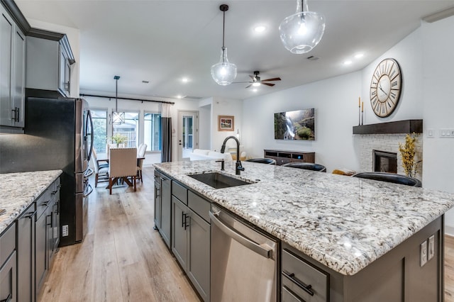 kitchen featuring gray cabinets, hanging light fixtures, appliances with stainless steel finishes, a sink, and an island with sink