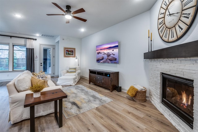 living area with light wood-style flooring, a fireplace, visible vents, and baseboards