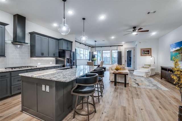 kitchen featuring a large island, hanging light fixtures, appliances with stainless steel finishes, open floor plan, and wall chimney range hood