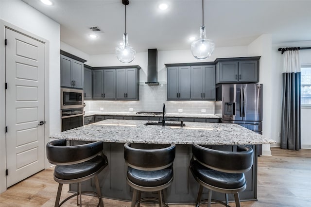 kitchen featuring visible vents, an island with sink, wall chimney exhaust hood, appliances with stainless steel finishes, and a sink