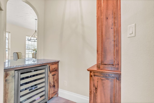 bar featuring hanging light fixtures, wine cooler, baseboards, and arched walkways