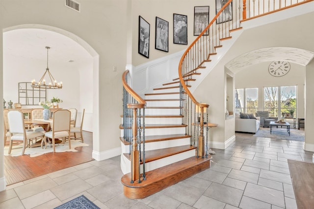 foyer with visible vents, arched walkways, a towering ceiling, stairs, and a notable chandelier