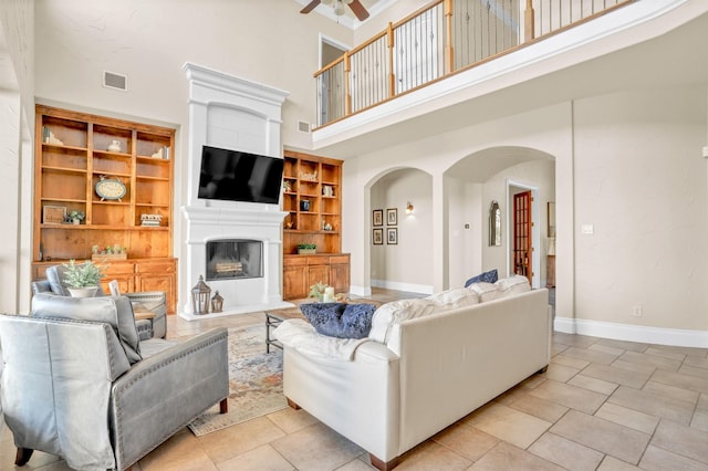 living room featuring visible vents, arched walkways, baseboards, ceiling fan, and a fireplace