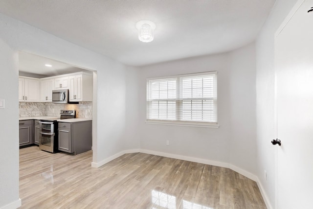 kitchen with baseboards, stainless steel appliances, light countertops, light wood-type flooring, and backsplash