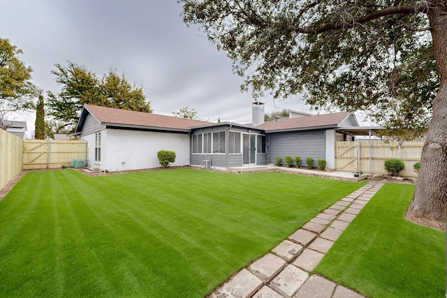 rear view of property with a sunroom, a fenced backyard, a lawn, and a chimney