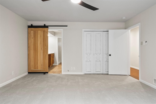 unfurnished bedroom featuring ensuite bathroom, a barn door, light carpet, baseboards, and a closet