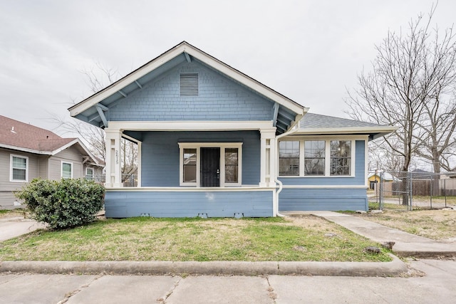 bungalow with covered porch, fence, and a front yard