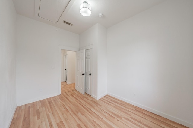 empty room with attic access, visible vents, light wood-style flooring, and baseboards