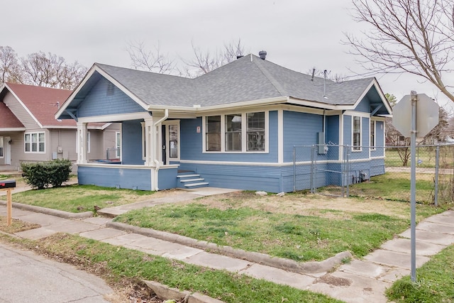 view of front of home with a shingled roof, a porch, a front yard, and fence