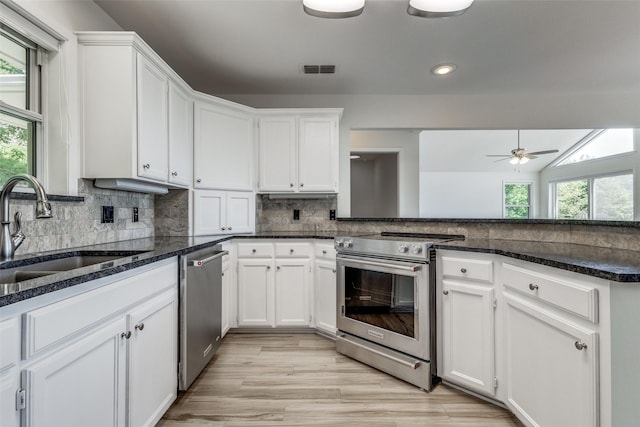 kitchen featuring stainless steel appliances, decorative backsplash, white cabinets, a sink, and dark stone countertops