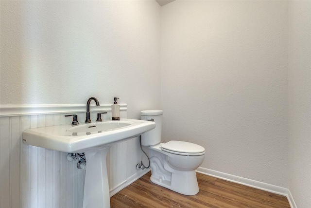 half bath featuring toilet, a sink, baseboards, and wood finished floors