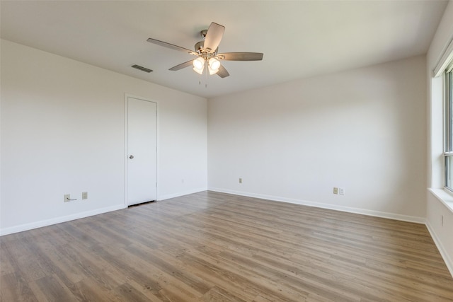 unfurnished room with a ceiling fan, wood finished floors, visible vents, and baseboards