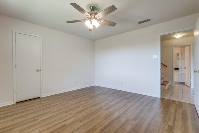 empty room featuring light wood-style flooring, visible vents, a ceiling fan, stairs, and baseboards