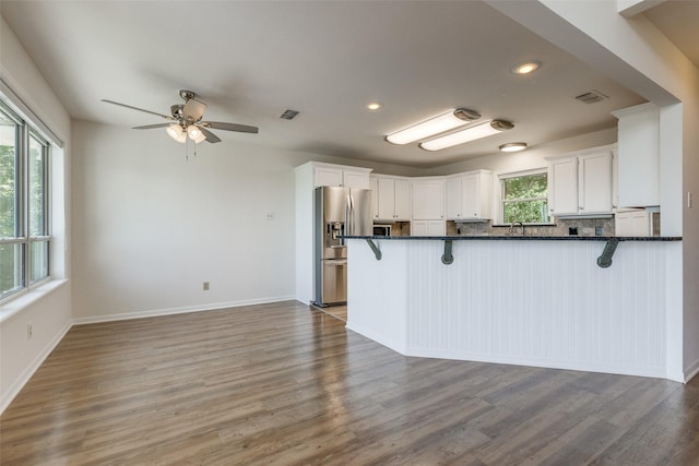 kitchen with a peninsula, visible vents, white cabinetry, and stainless steel refrigerator with ice dispenser