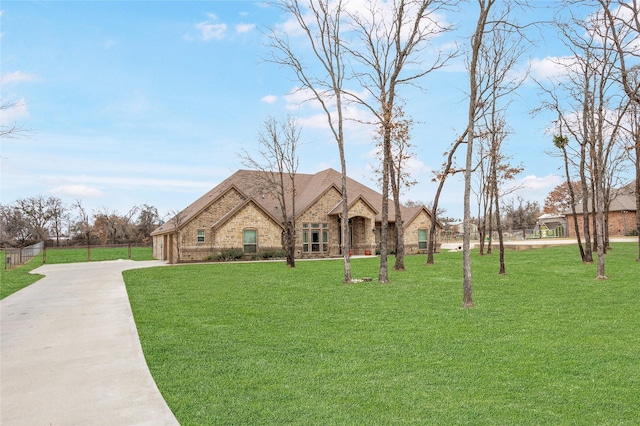 french country home with stone siding, a front lawn, concrete driveway, and brick siding