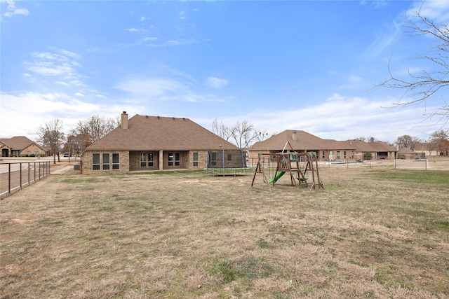 back of house featuring a lawn, a fenced backyard, a chimney, a trampoline, and a playground