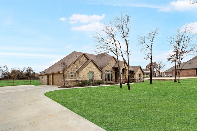 french country home featuring an attached garage, concrete driveway, stone siding, and a front yard