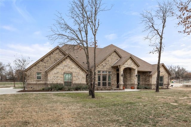 french country inspired facade with brick siding, a front yard, fence, and a shingled roof