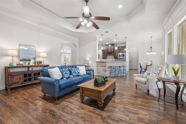 living area with crown molding, a tray ceiling, arched walkways, and dark wood-style flooring