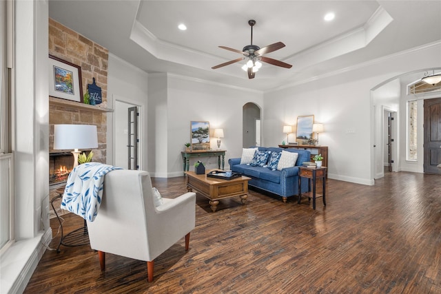 living room featuring crown molding, arched walkways, a raised ceiling, and dark wood-type flooring