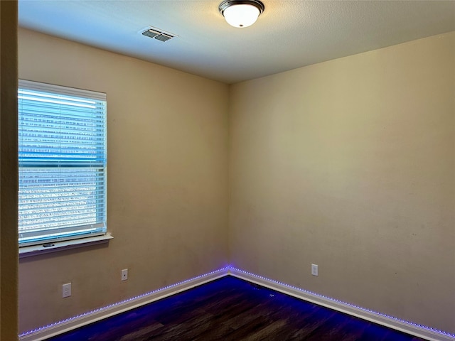 empty room with dark wood-style floors, a healthy amount of sunlight, visible vents, and baseboards