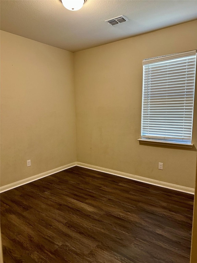 unfurnished room featuring dark wood-style flooring, visible vents, a textured ceiling, and baseboards