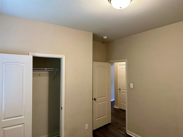 unfurnished bedroom featuring dark wood-style floors, a closet, a textured ceiling, and baseboards