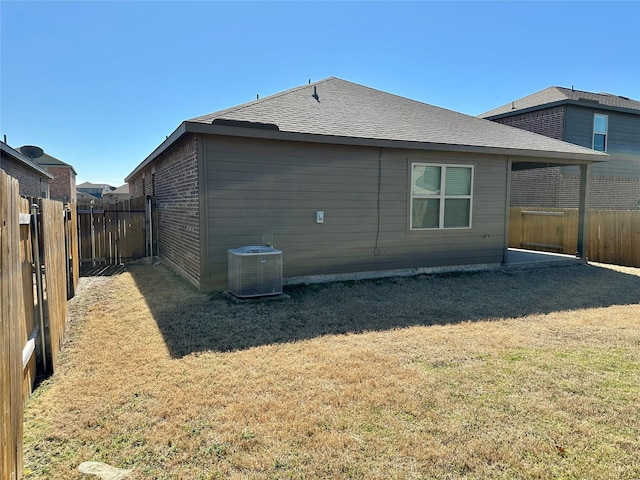 back of house with roof with shingles, a fenced backyard, a lawn, and central AC unit