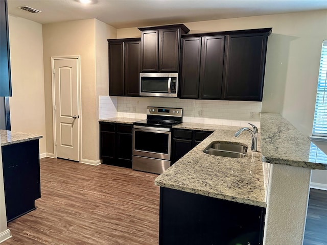 kitchen featuring stainless steel appliances, visible vents, a sink, wood finished floors, and a peninsula