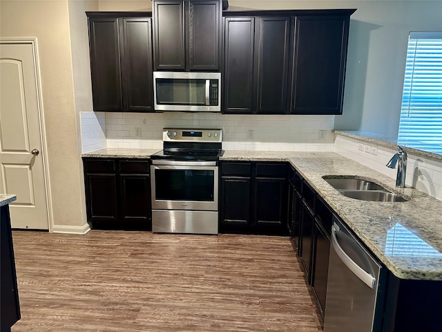 kitchen with wood finished floors, a sink, light stone countertops, stainless steel appliances, and backsplash