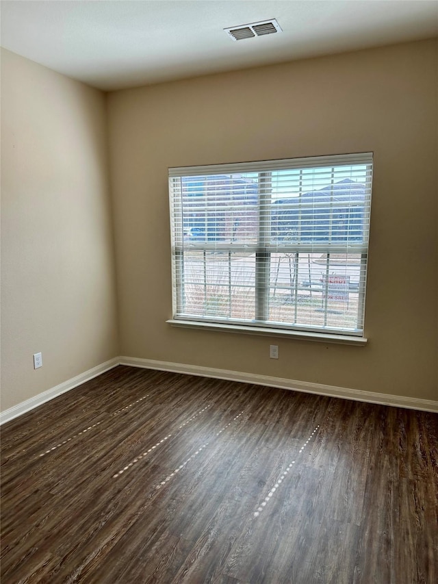 empty room with dark wood-style floors, visible vents, and baseboards