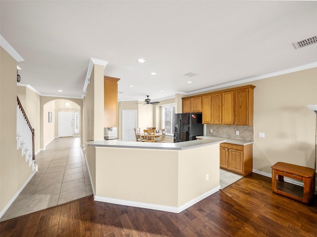 kitchen with arched walkways, visible vents, black refrigerator with ice dispenser, wood-type flooring, and tasteful backsplash