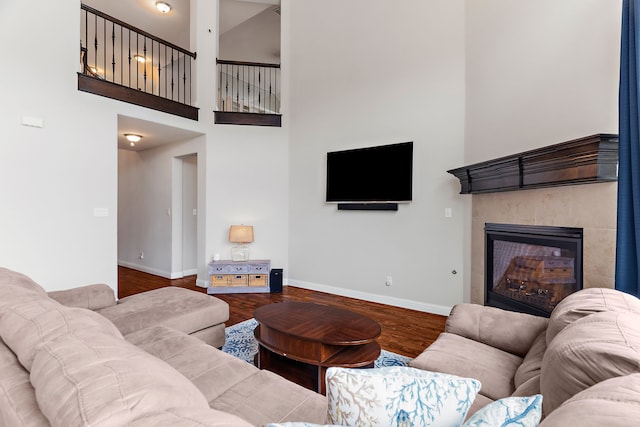 living room featuring a high ceiling, a fireplace, baseboards, and wood finished floors