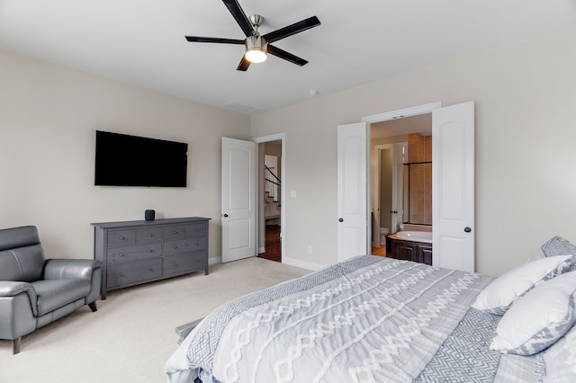 bedroom featuring baseboards, ceiling fan, ensuite bathroom, and light colored carpet