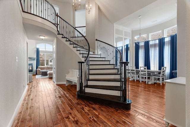 entrance foyer featuring baseboards, a glass covered fireplace, dark wood-style floors, stairway, and a chandelier