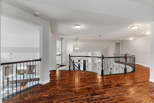 corridor featuring wood finished floors, baseboards, an upstairs landing, and an inviting chandelier