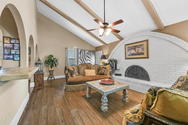 living area with dark wood-style flooring, a ceiling fan, baseboards, a brick fireplace, and beam ceiling