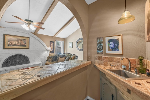 kitchen featuring tasteful backsplash, tile countertops, decorative light fixtures, a fireplace, and a sink