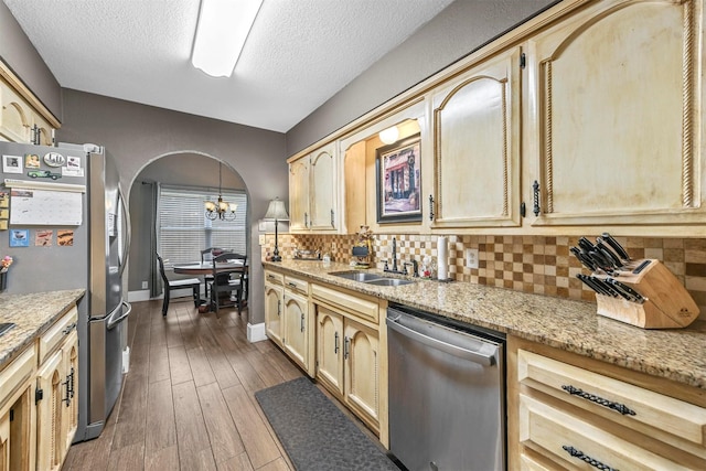 kitchen featuring arched walkways, dark wood-style flooring, backsplash, appliances with stainless steel finishes, and a sink