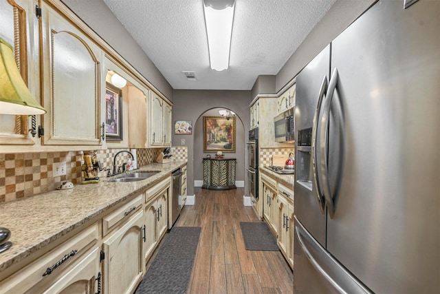 kitchen with arched walkways, a sink, visible vents, appliances with stainless steel finishes, and dark wood finished floors