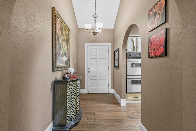 foyer with baseboards, arched walkways, lofted ceiling, wood finished floors, and a notable chandelier